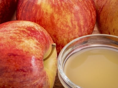 unfiltered, raw apple cider vinegar with mother - a small galls bowl surrounded by fresh red apples.