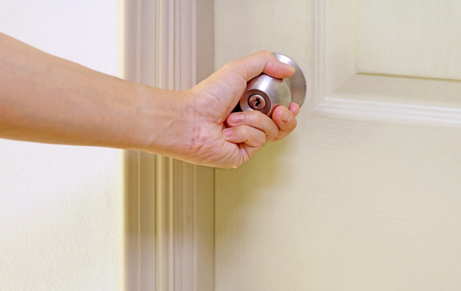 Man's Hand holding steel doorknob to open the door.