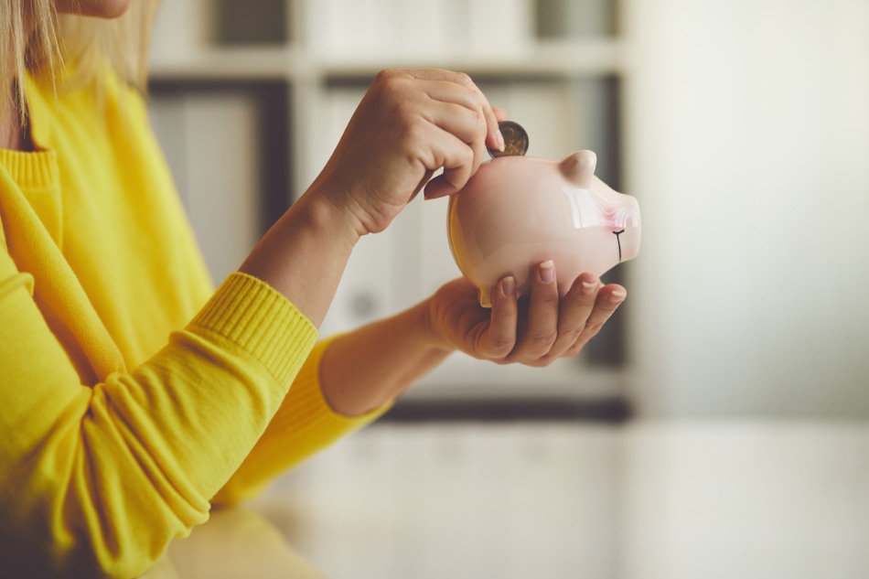 Woman inserts a coin into a piggy bank.