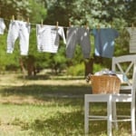 Wicker basket on white chair and baby laundry hanging on clothesline.