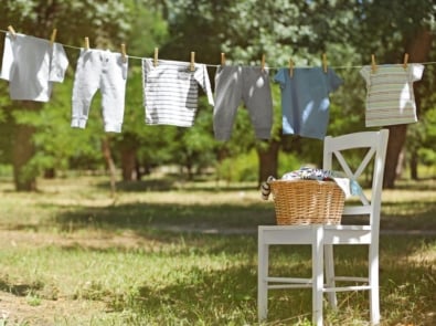 Wicker basket on white chair and baby laundry hanging on clothesline.