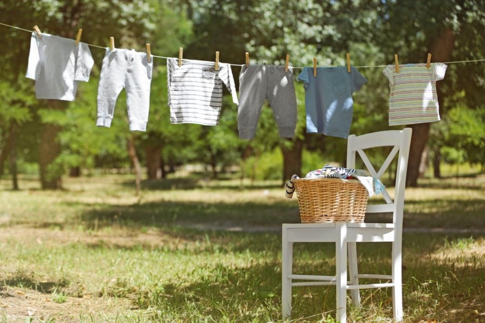 Wicker basket on white chair and baby laundry hanging on clothesline.