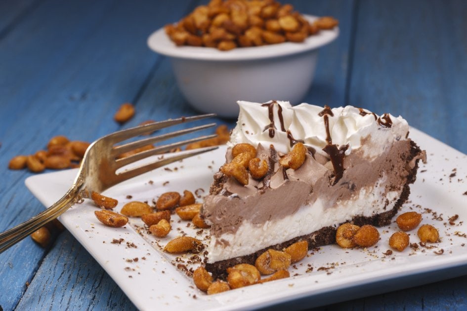 A studio image of a slice of ice cream pie along with peanuts.