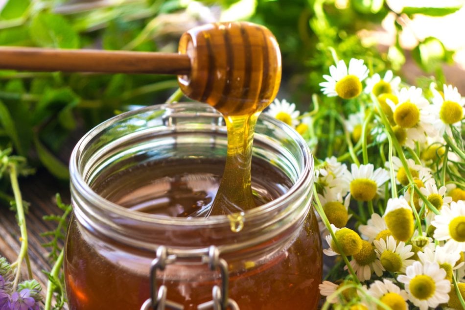 Close up of a jar of local honey with wildflowers in the background