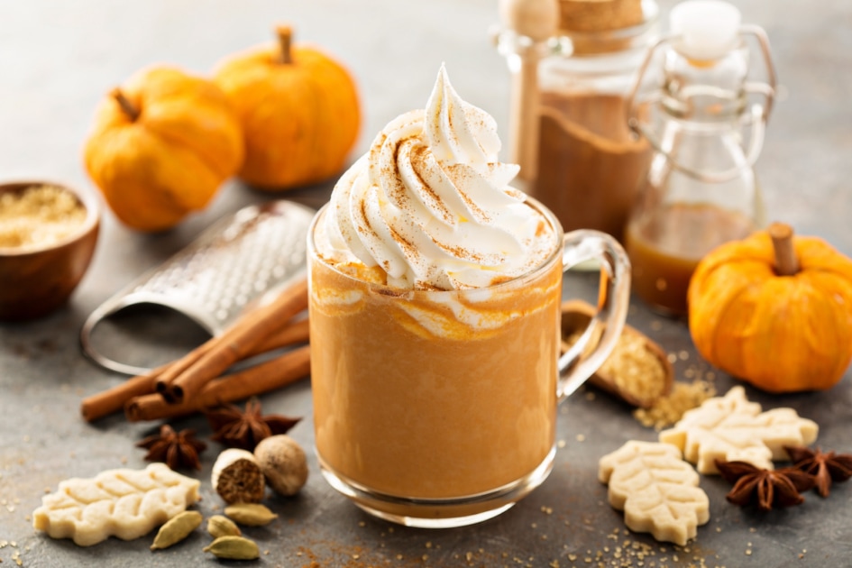 Pumpkin spice latte in a glass mug with cinnamon, nutmeg and cookies.