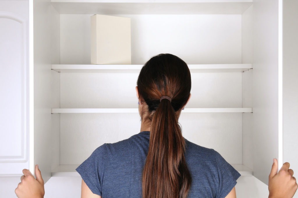 Closeup of a woman looking in an empty pantry. Seen from behind there is only one box of food. Horizontal format.