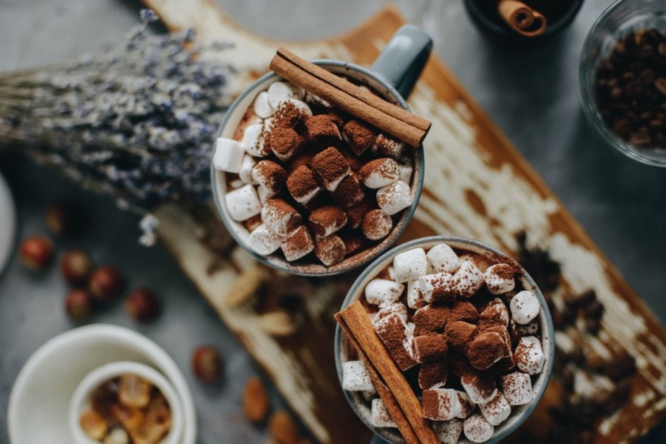 Two cups of hot cocoa with marshmallows and cinnamon, view from above.