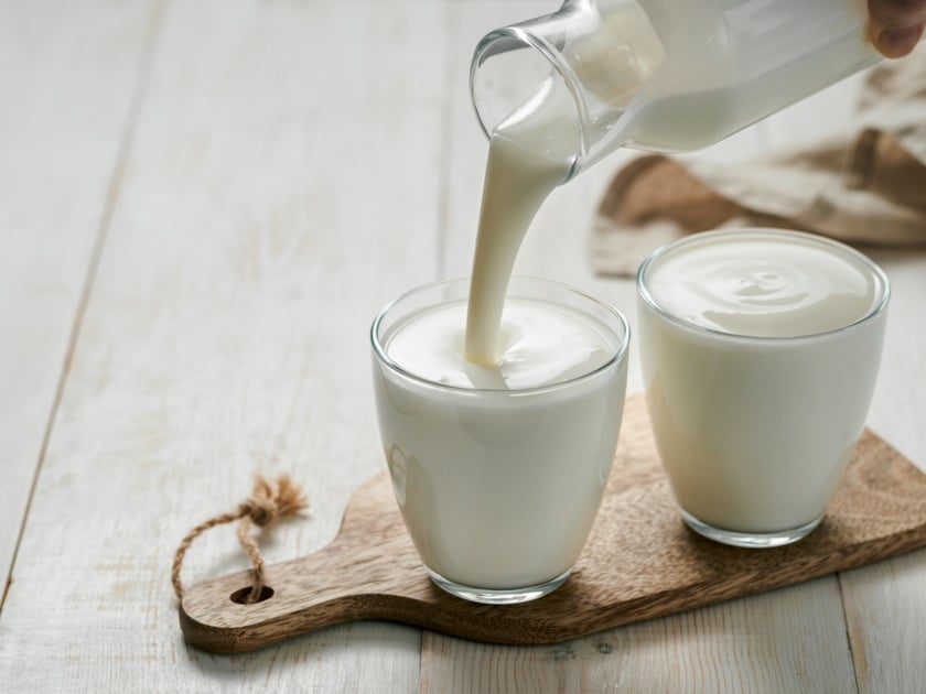 Pouring homemade kefir, buttermilk or yogurt with probiotics. Yogurt flowing from glass bottle on white wooden background. Probiotic cold fermented dairy drink. Trendy food and drink.