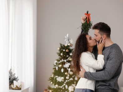 Happy couple kissing under mistletoe bunch in room decorated for Christmas.