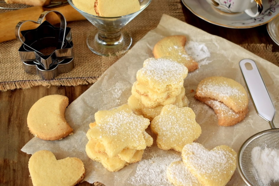 Shaped shortbread cookies covered with sugar powder surrounded by kitchen utensils.