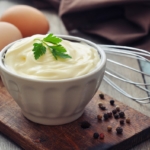 Homemade mayonnaise on wooden board with eggs in background.
