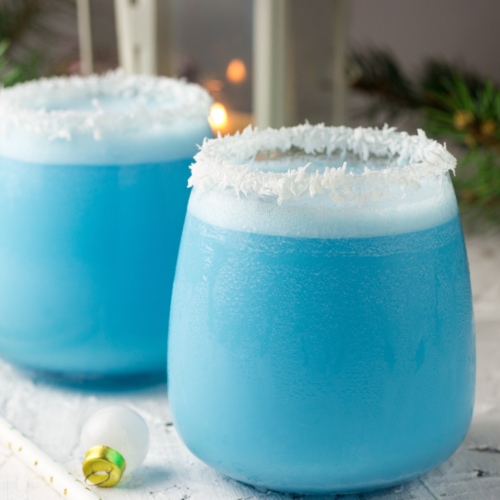 Blue curacao Christmas Cocktail, garnished with coconut on Christmas decorated holiday table with Christmas ornaments. Holiday cocktails with ice Blue Curacao, coconut cream, vodka and pineapple juice.