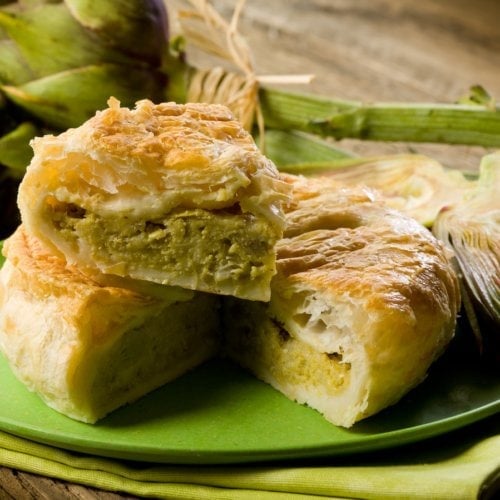 Artichoke pie on green plate on wooden table.