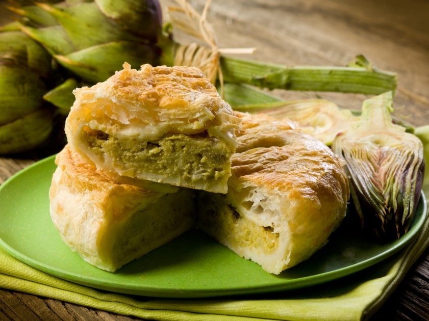 Artichoke pie on green plate on wooden table.