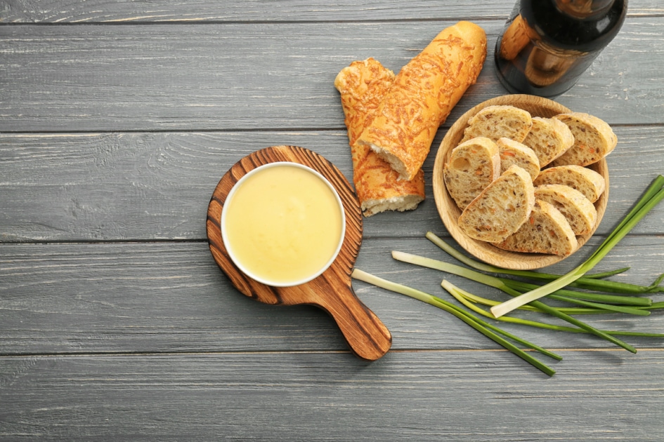 Bowl with beer cheese dip and bread on wooden background.