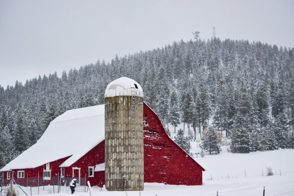 Snowy scene with red barn in foreground.