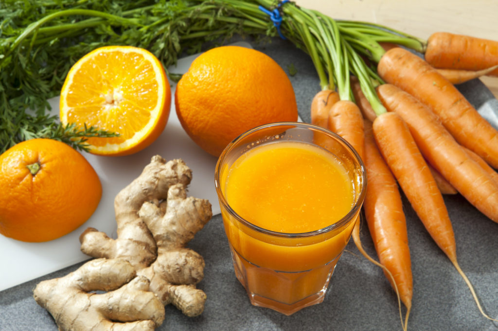 Glass of fruit juice with orange, carrots and ginger on a cutting board