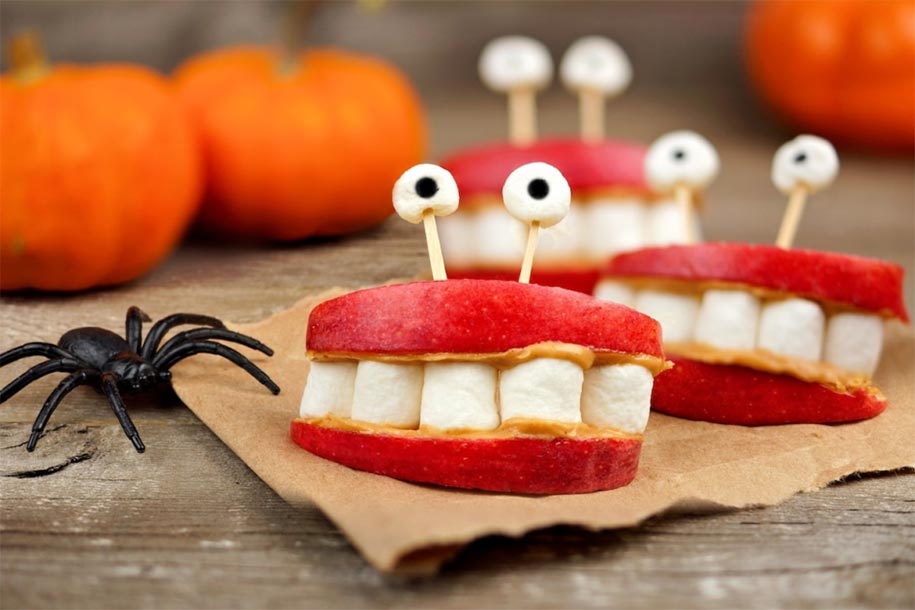 Healthy Halloween apple, marshmallow, peanut butter monster teeth on a rustic wooden background.