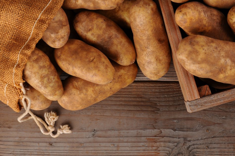 A burlap sack of potatoes and a wooden crate on a rustic wooden background. Overhead shot in horizontal format with copy space.