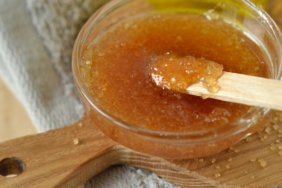 Close-up of homemade lip scrub made out of brown sugar, honey and olive oil in glass bowl on wooden chopping board - Natural beauty product.
