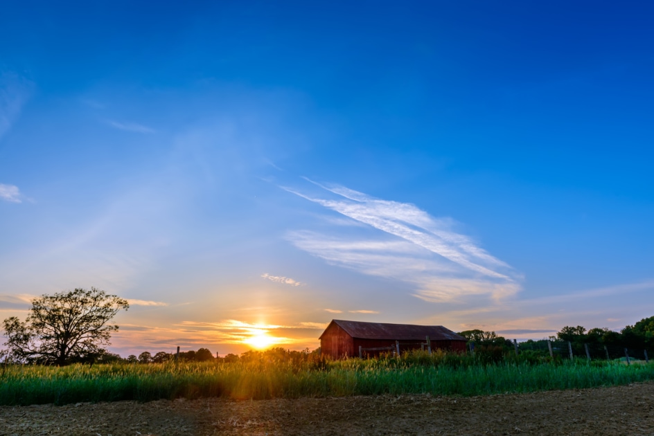 Deep blue sky with sun setting behind a barn.