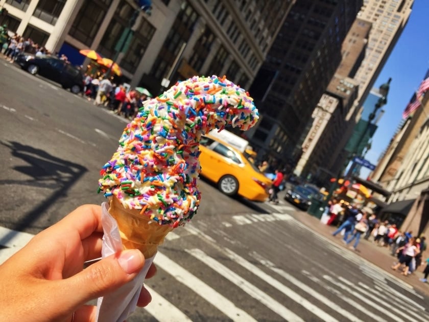 Hand holding ice cream cone with rainbow sprinkles on a city street
