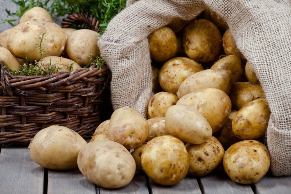 Sack of potatoes spilling onto wooden floor.