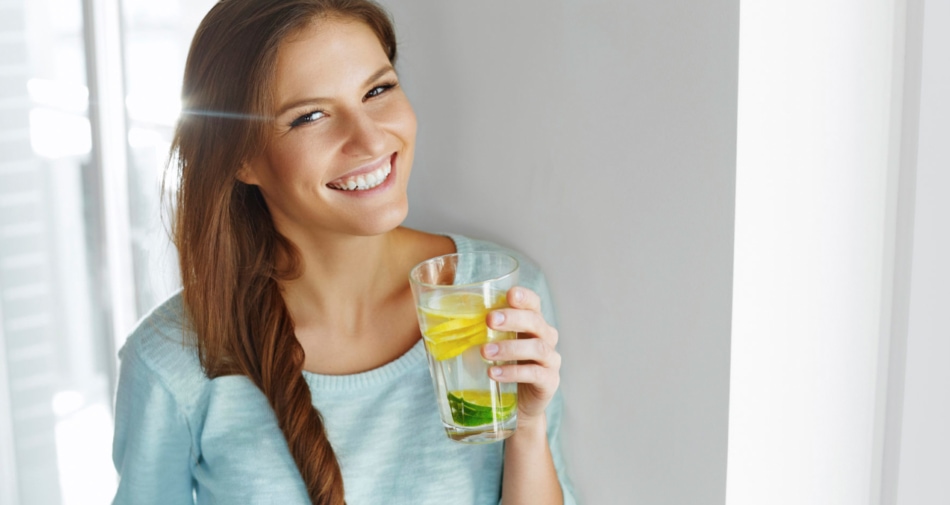 Woman smiling while holding a glass of lemon flavored water.