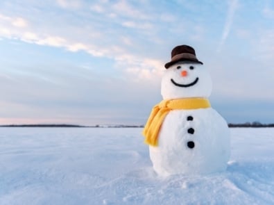 Funny snowman in stylish hat and yellow scarf on snowy field.