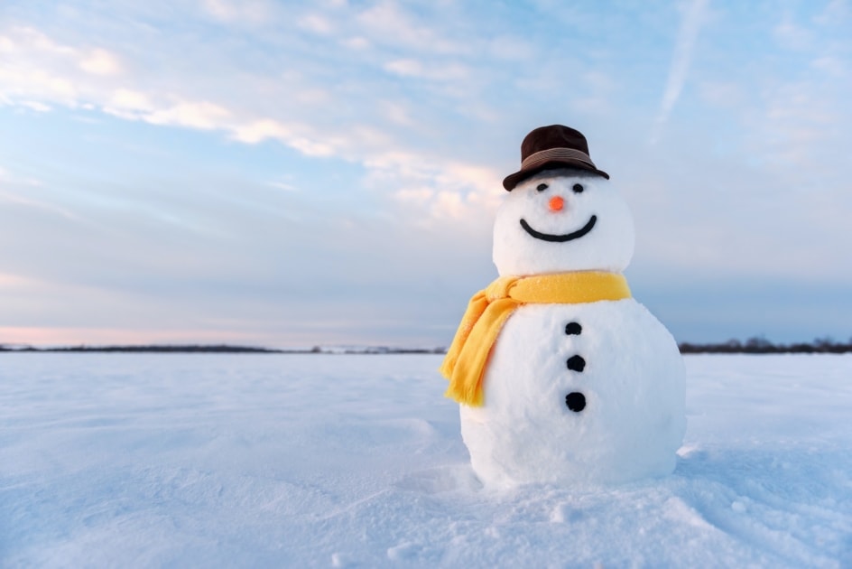 Funny snowman in stylish hat and yellow scarf on snowy field.