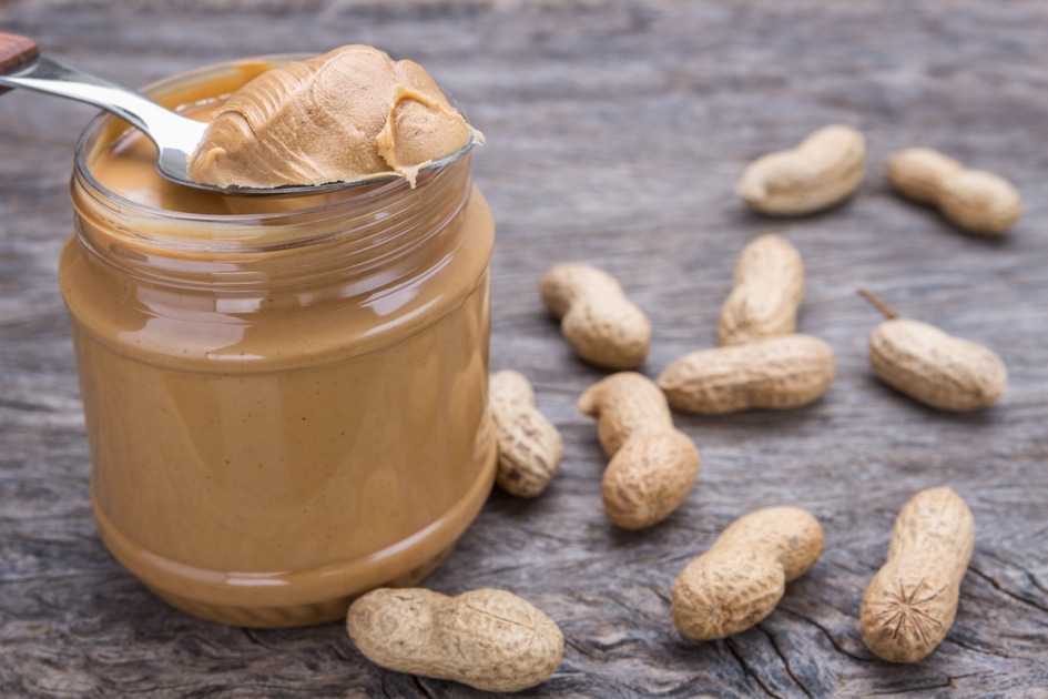 Jar of peanut butter with nuts. On wooden texture.