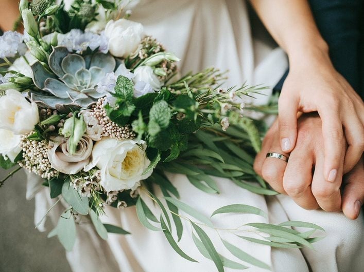 A wedding bouquet beside a married couple holding hands.