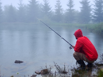 Man in red jacket fishing at a lake in the rain.