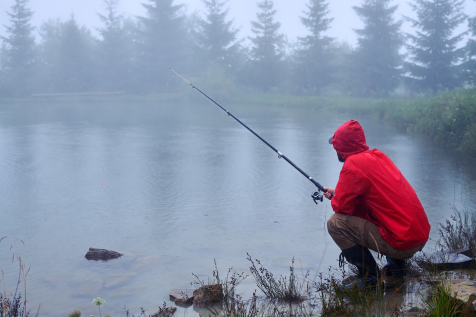 Man in red jacket fishing at a lake in the rain.