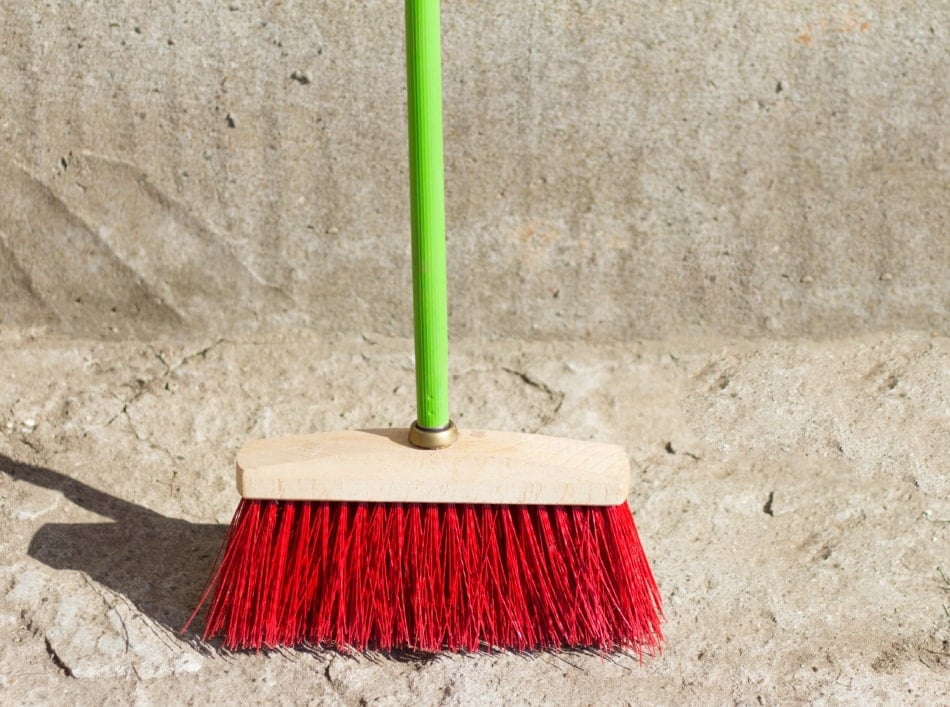 a large broom for street cleaning stands at the concrete wall on the asphalt