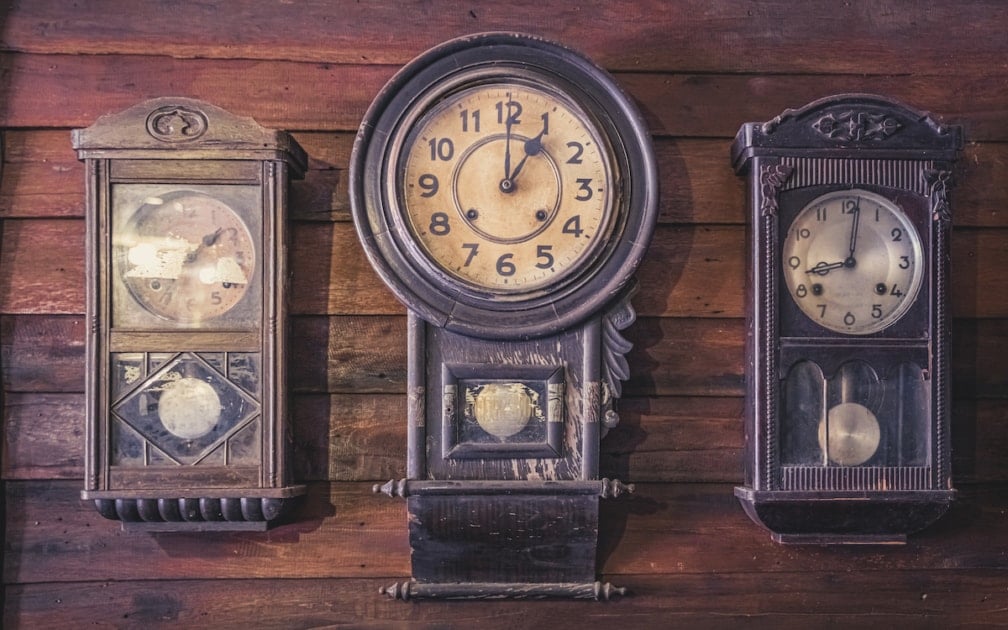 Three antique clocks on a varnished wooden wall.