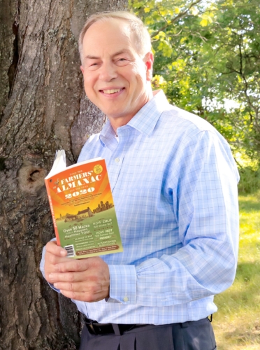 Peter Geiger holding the 2020 Farmers' Almanac by a tree.