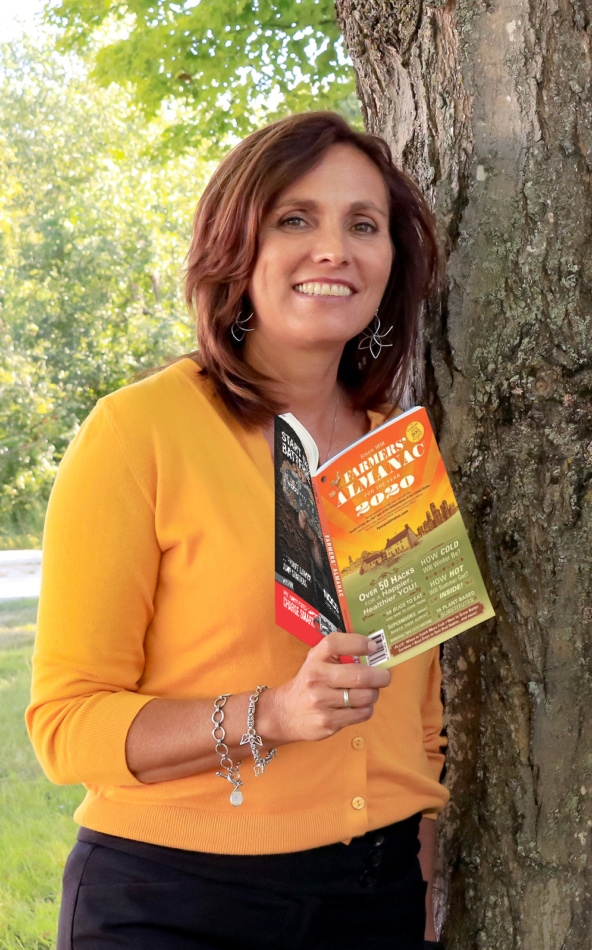 Sandi Duncan, Farmers Almanac Editor, holding a copy of the 2020 Farmers' Almanac by a tree.