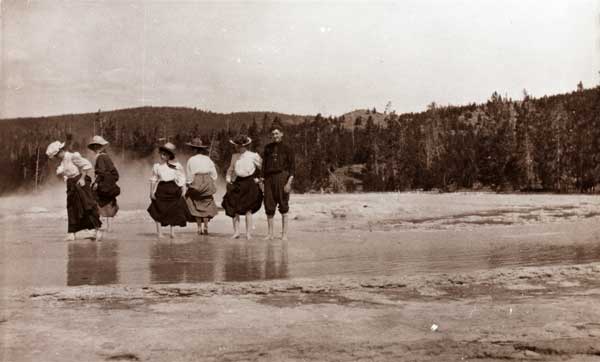 Three women and a man walk barefoot across a shallow pool at Warm Eagle Rock, Yosemite National Park, 1902