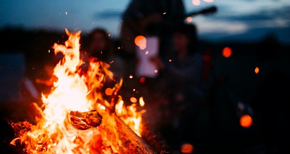 Bonfire with silhouette of a man playing guitar in background.