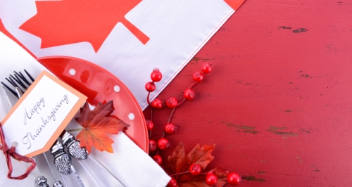 Happy Thanksgiving tag over silverware, plates and a red tablecloth depicting the Canadian flag.