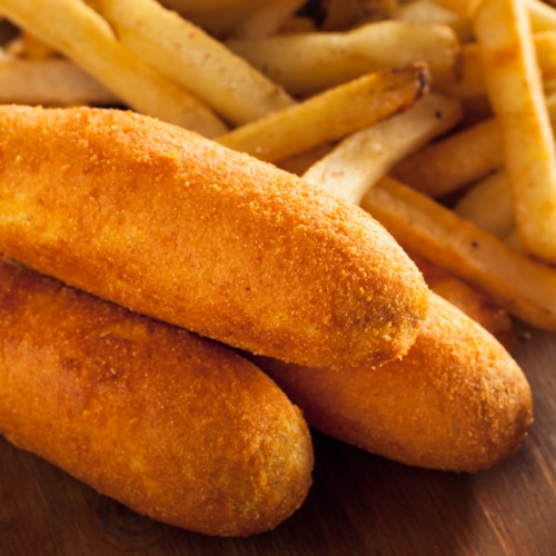 A stack of corn dogs next to french fries.