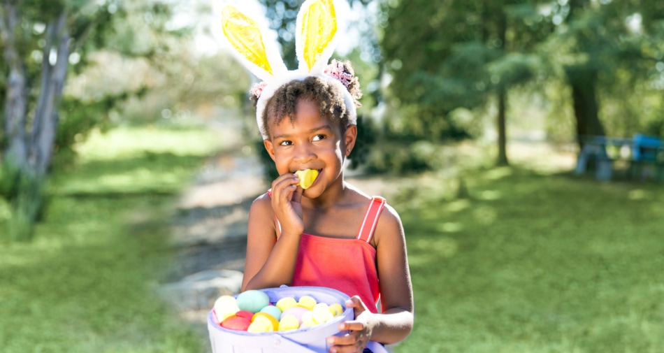 Young girl wearing bunny ears enjoying a basket of Easter candy.