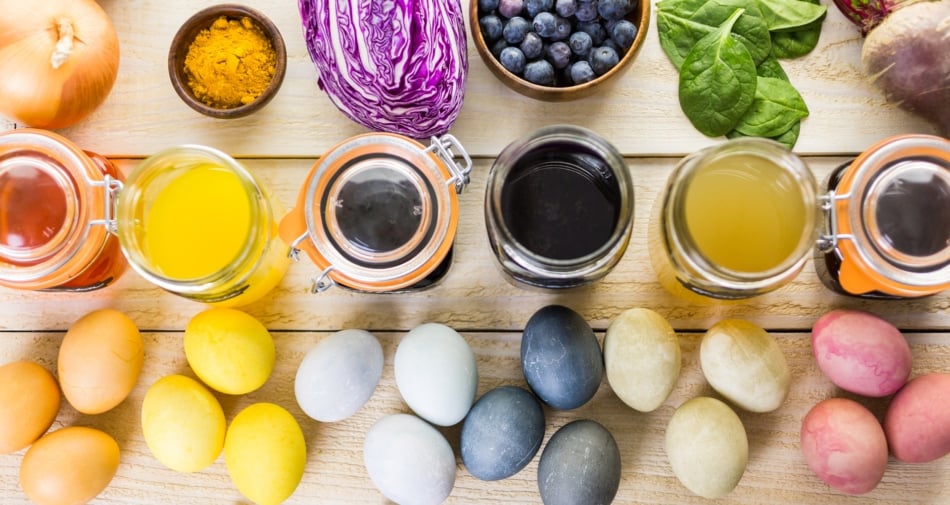 Dyed Easter eggs on table in variety of colors next to coloring jars.