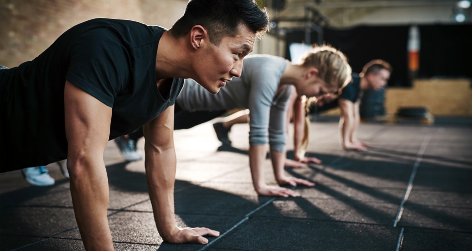 Asian man doing pushups in a gym with a group of others.