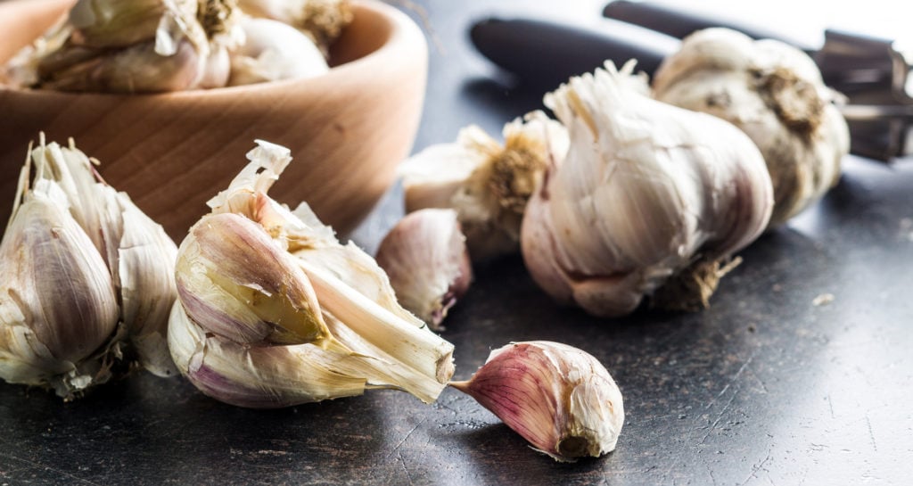 garlic bulbs near a bowl, with one garlic broken up