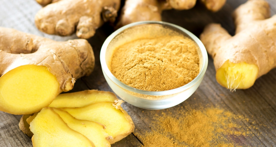 Bowl of powdered ginger surrounded by ginger roots.