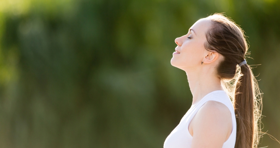 Woman closing eyes and looking content up at sky with blurred trees in background.