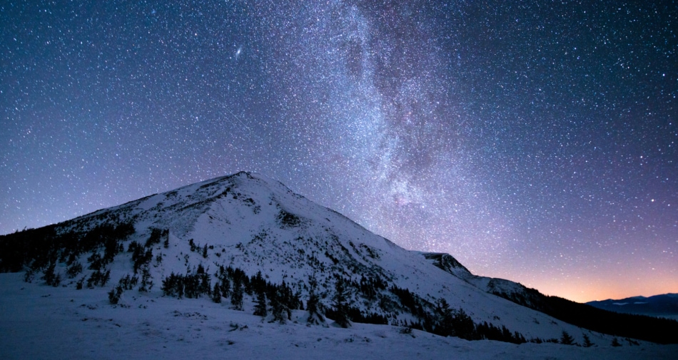 Milky Way appearing over snowy mountains with a pink hue.