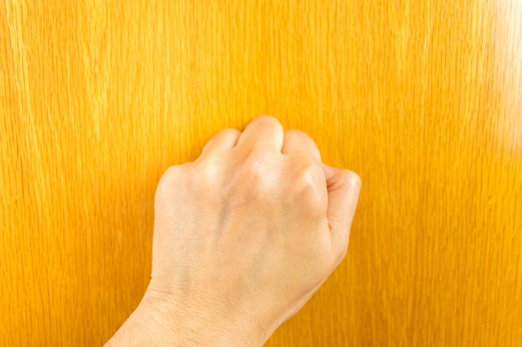 view of hand knocking the wooden door.